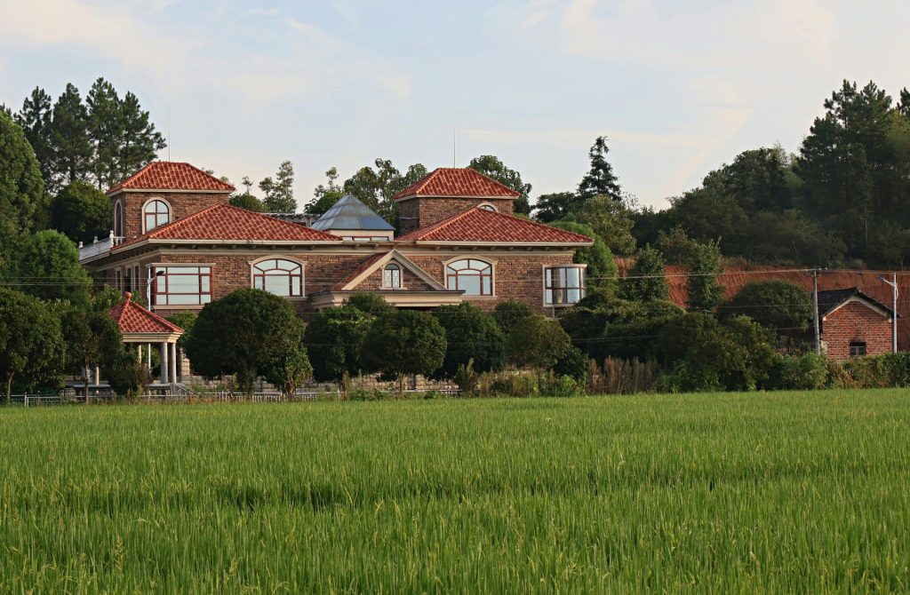 Large brick house with red tile roofs surrounded by greenery.