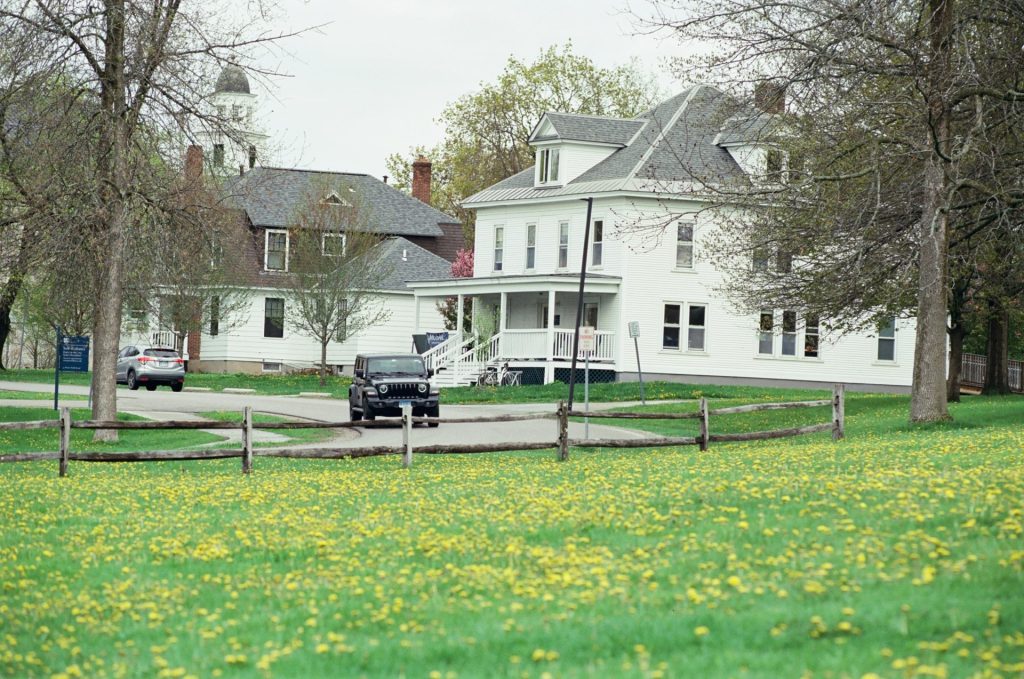 White houses and cars on a street with green field.