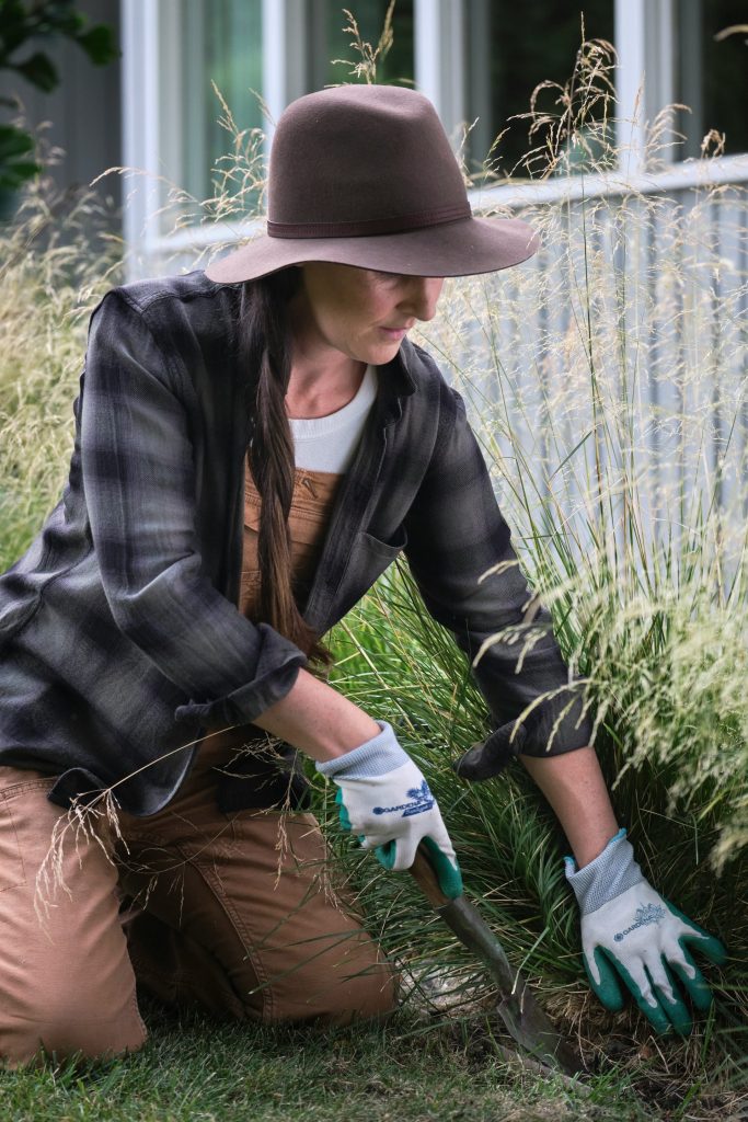 A woman in a hat and gloves working in the grass